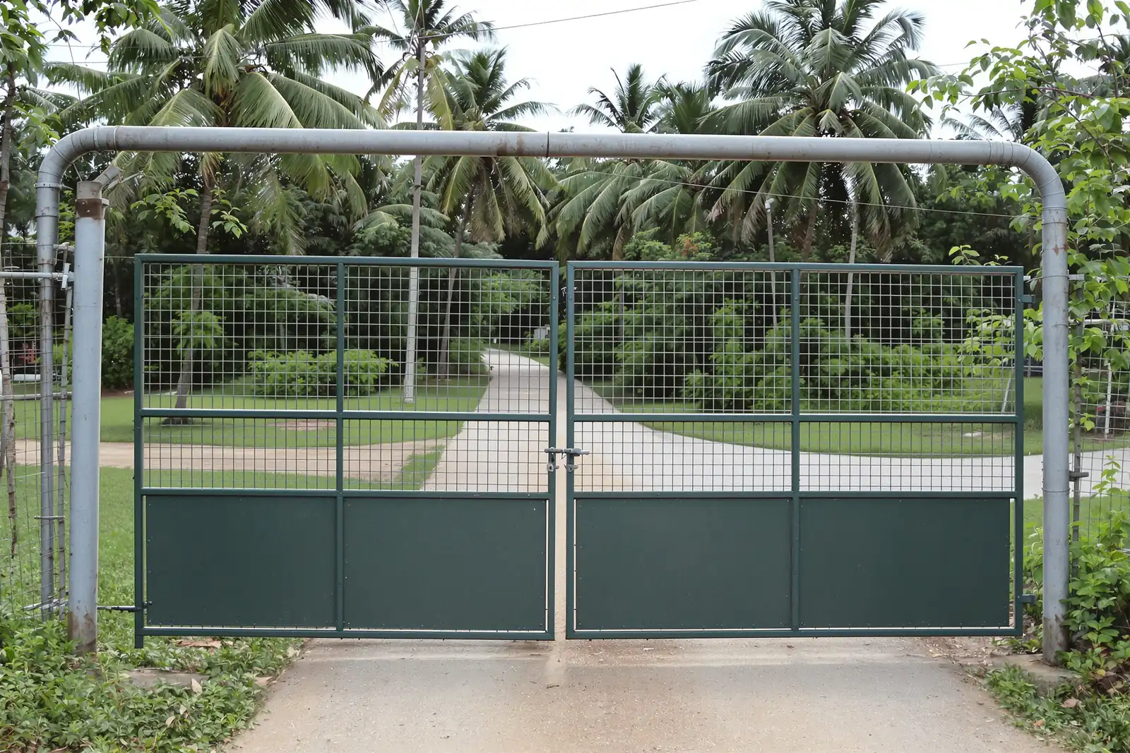 Green pipe-frame farm gate with welded mesh at a rural driveway